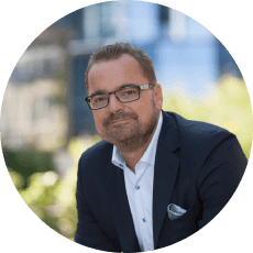 Natural Pharmaceuticals VitaSolaris® D3 Mees tumedas ülikonnas ja prillidega naeratab linnataustaga väljas foto.